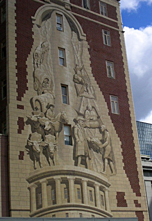 [A mural with a wagon train up the left side with oxen pulling it. On the right side are native amercians and teepees.]